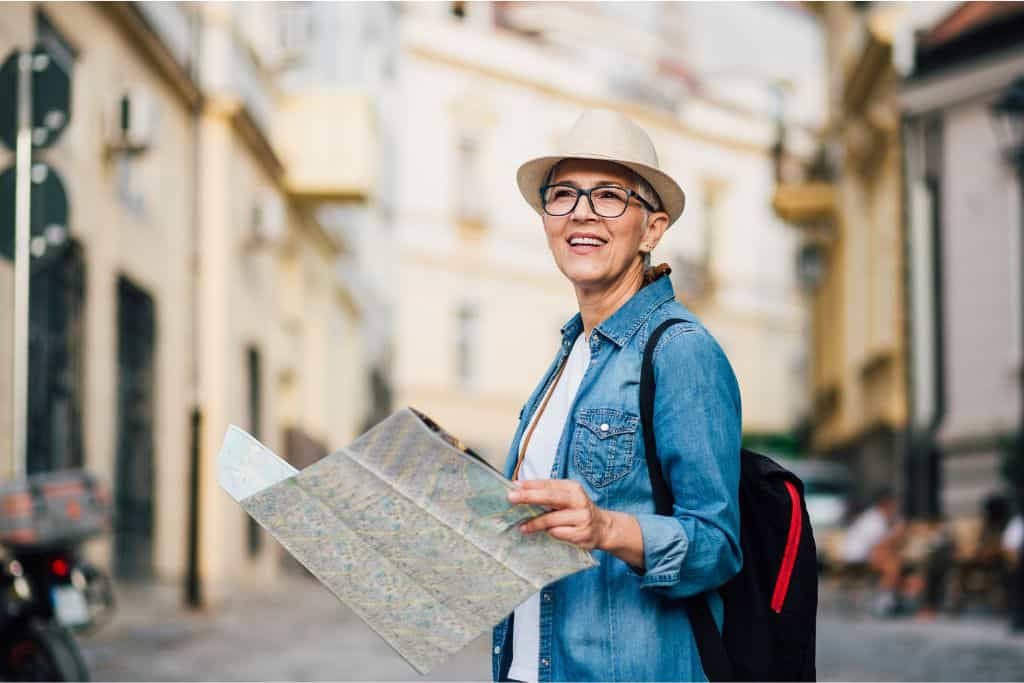 Older digital nomad waking with a map in what appears to be a European city.