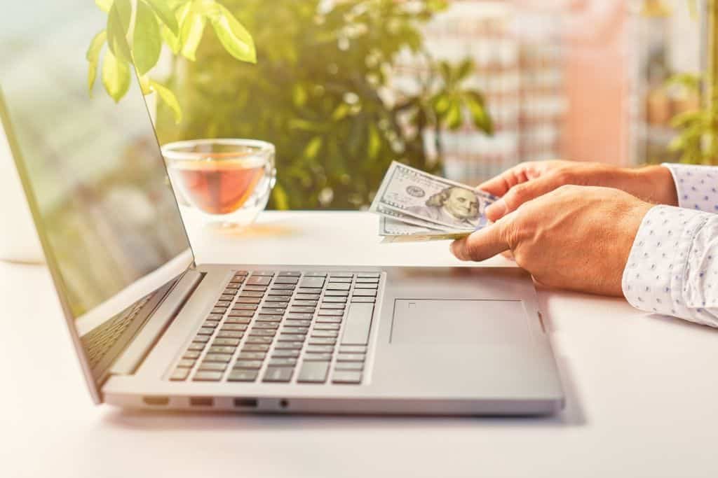 Person with cash next to a laptop.