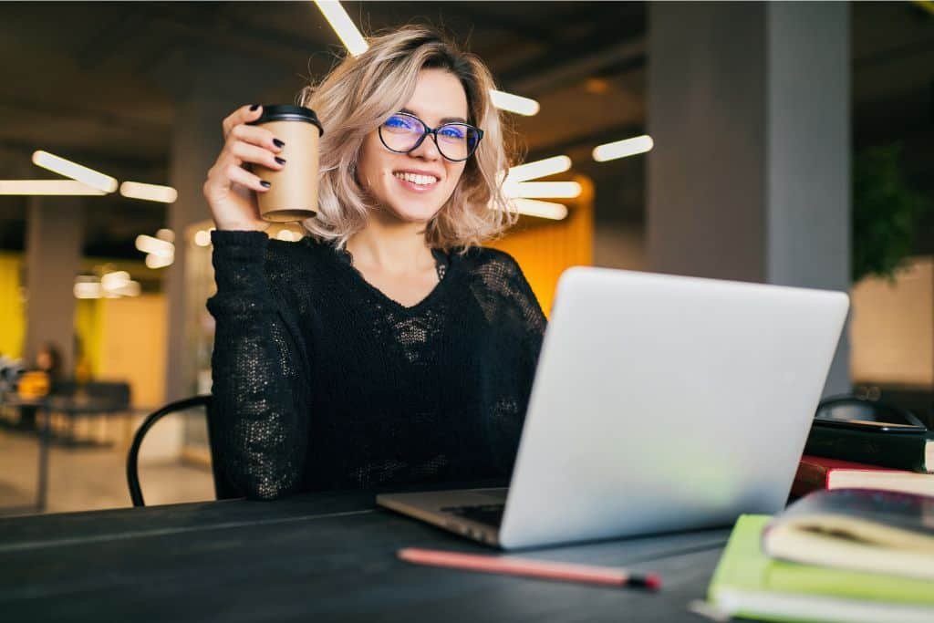 A woman drinking coffee working on a laptop.