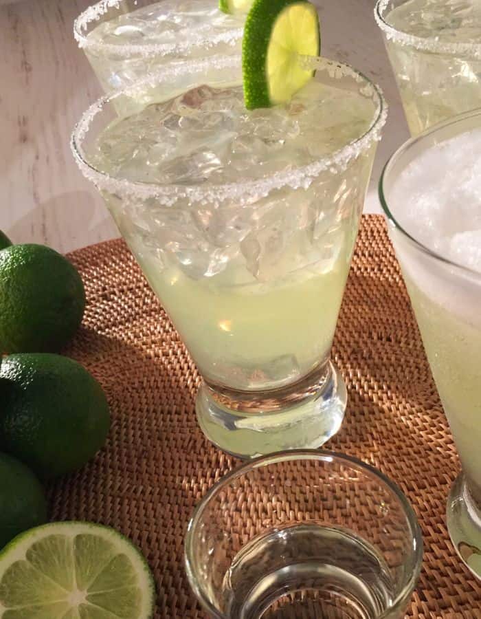 A margarita with salted rim and a lime wedge. There are also limes on the table.