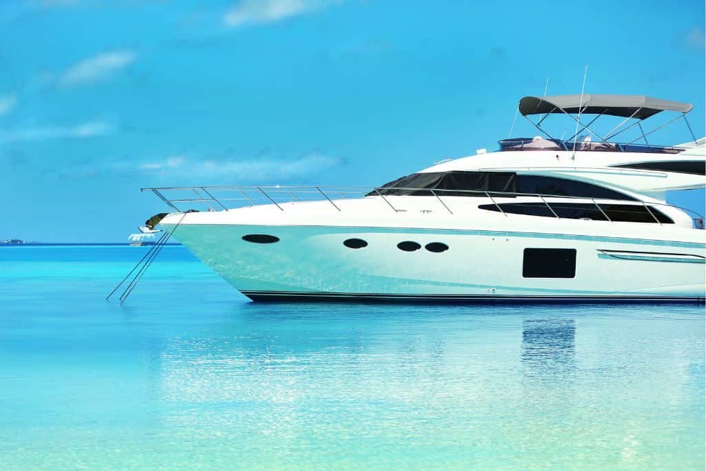 Sleek white luxury yacht anchored in the calm, crystal-clear turquoise waters off Cozumel, with a swim ladder extended and a bright blue sky above.