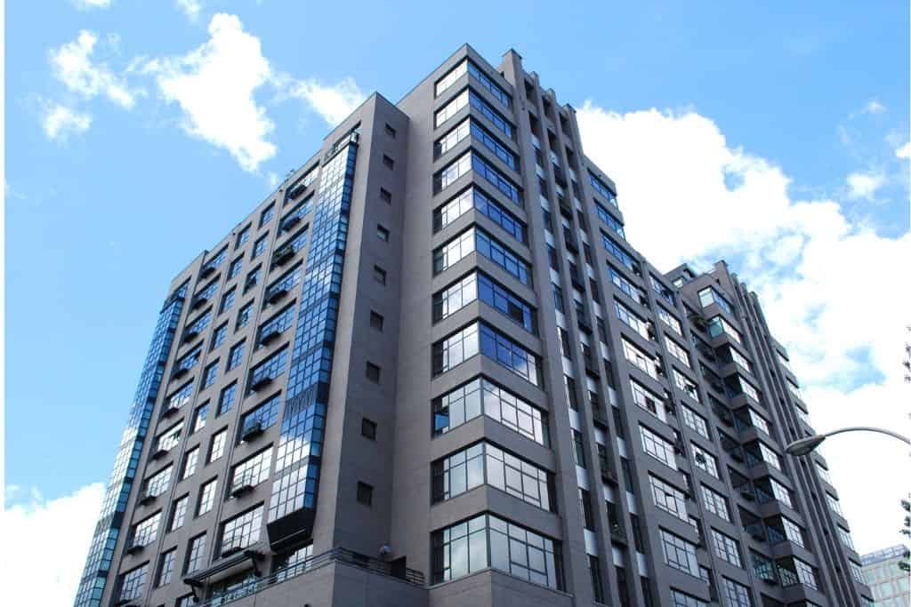 ChatGPT said:
The image shows a modern high-rise apartment building with gray exterior walls and large reflective windows. The structure has multiple levels with varied window sizes and balconies. A bright blue sky with scattered clouds is visible in the background.