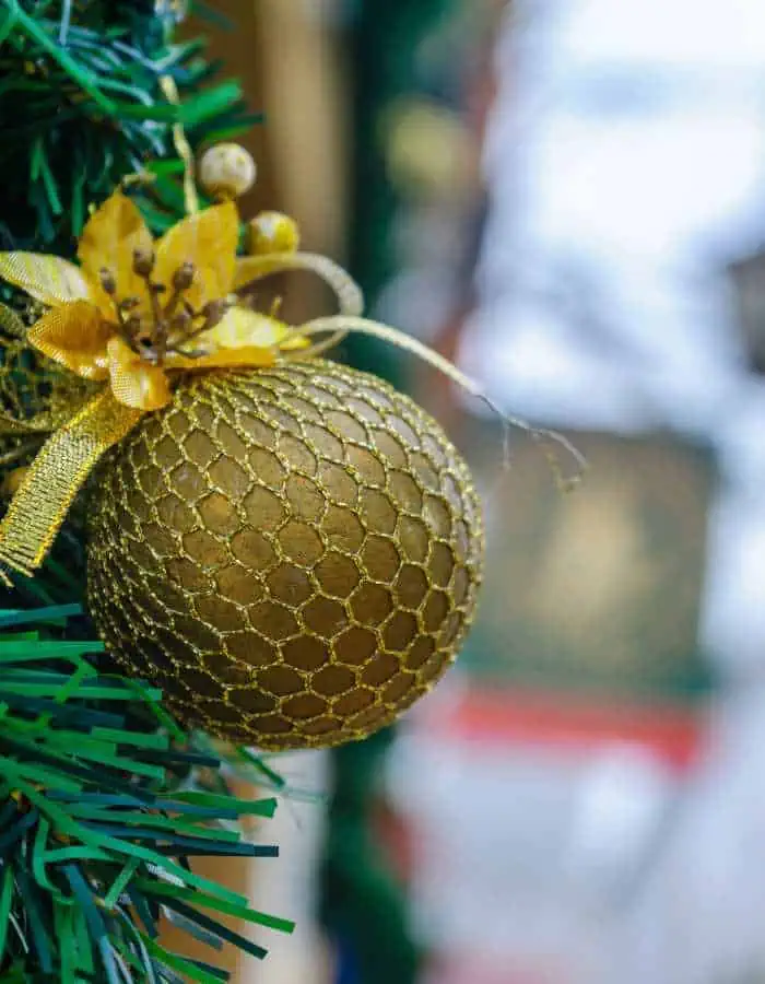 Christmas in Albufeira is captured in a close-up of a gold ornament with a mesh pattern and a decorative golden flower, hanging from green garland. The blurred background hints at festive surroundings, bringing a touch of elegance to the holiday scene.