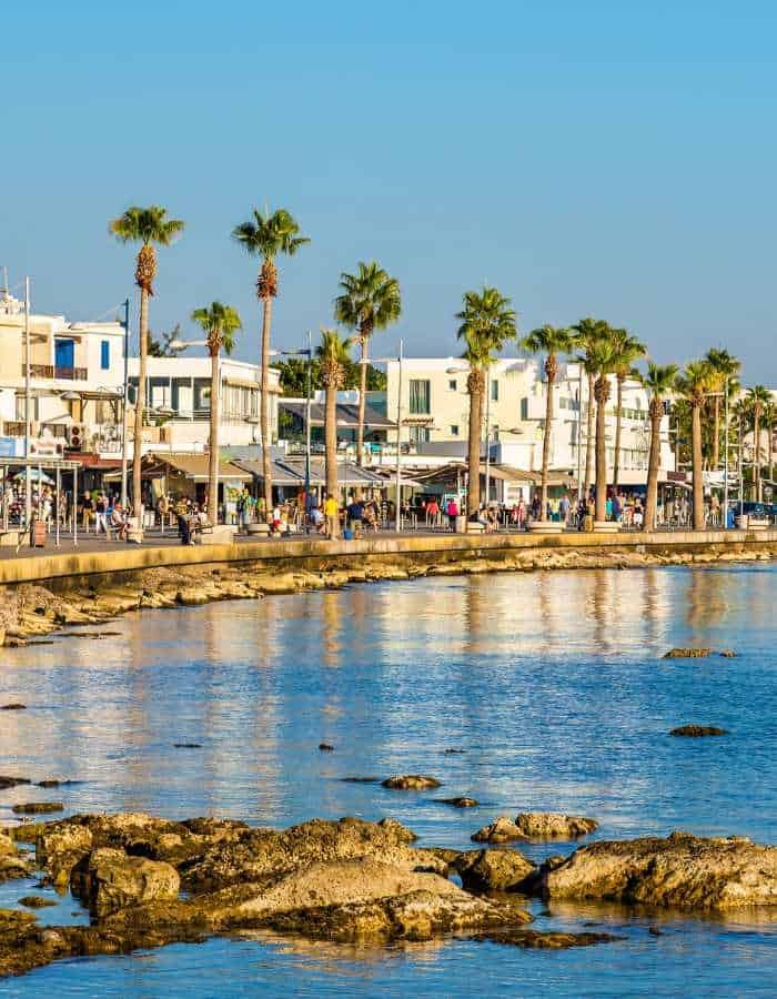 Christmas in Paphos offers a sunny coastal scene with palm trees lining the waterfront promenade, reflecting in the calm blue water. The festive atmosphere blends with the relaxed seaside charm, showing holiday cheer in a warm Mediterranean setting.