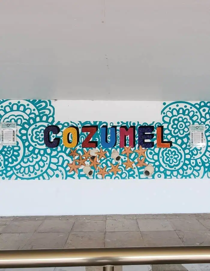 A colorful mural at Cozumel Airport spells out “COZUMEL” in bold, multicolored letters set against a teal floral background. Starfish and seashells are incorporated into the design, celebrating the island’s coastal charm and vibrant culture.