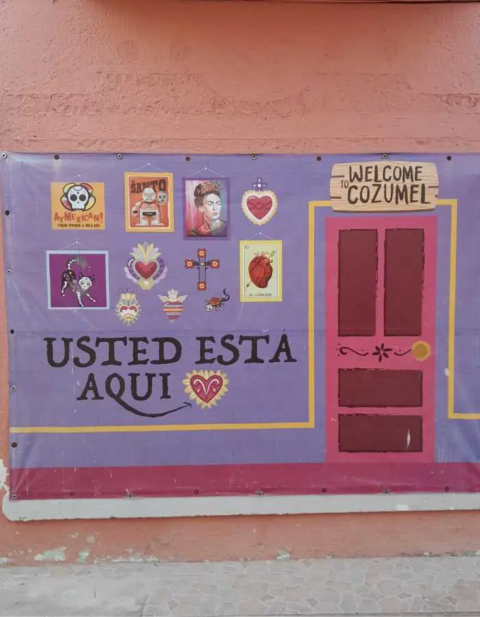 A sign that says "Usted esta aqui" with a drawing of a door and a sign that says "welcome to Cozumel"