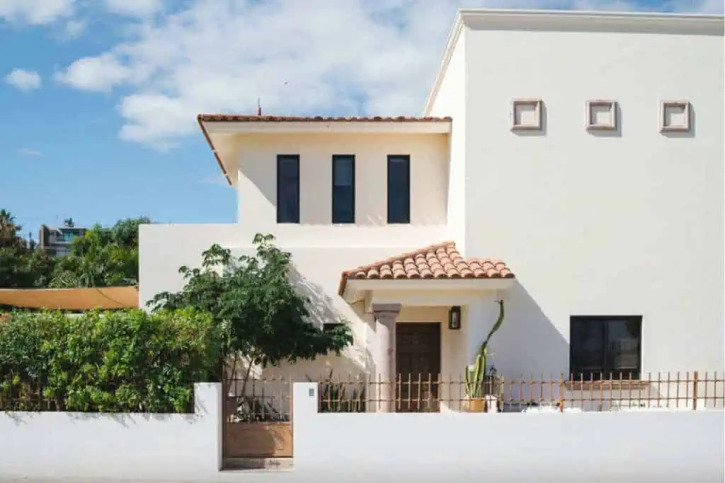 Exterior of a large, white house. It has a red tiled roof and trees in front.