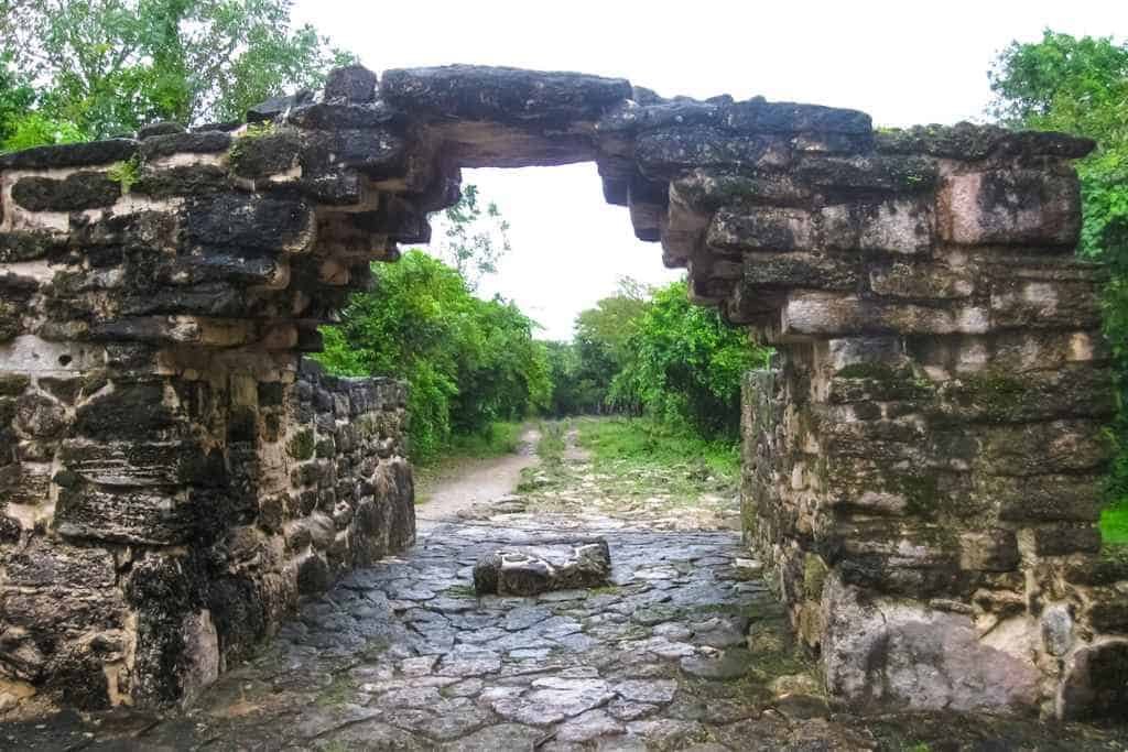 A stone archway with a road beyond that's lined with trees.