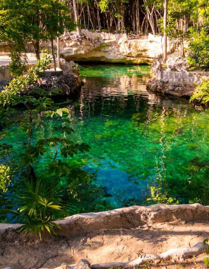 A tranquil cenote in the Yucatan Peninsula, surrounded by lush greenery and rocky outcrops, with crystal-clear waters revealing the natural underwater formations, a serene escape into nature's hidden wonders.