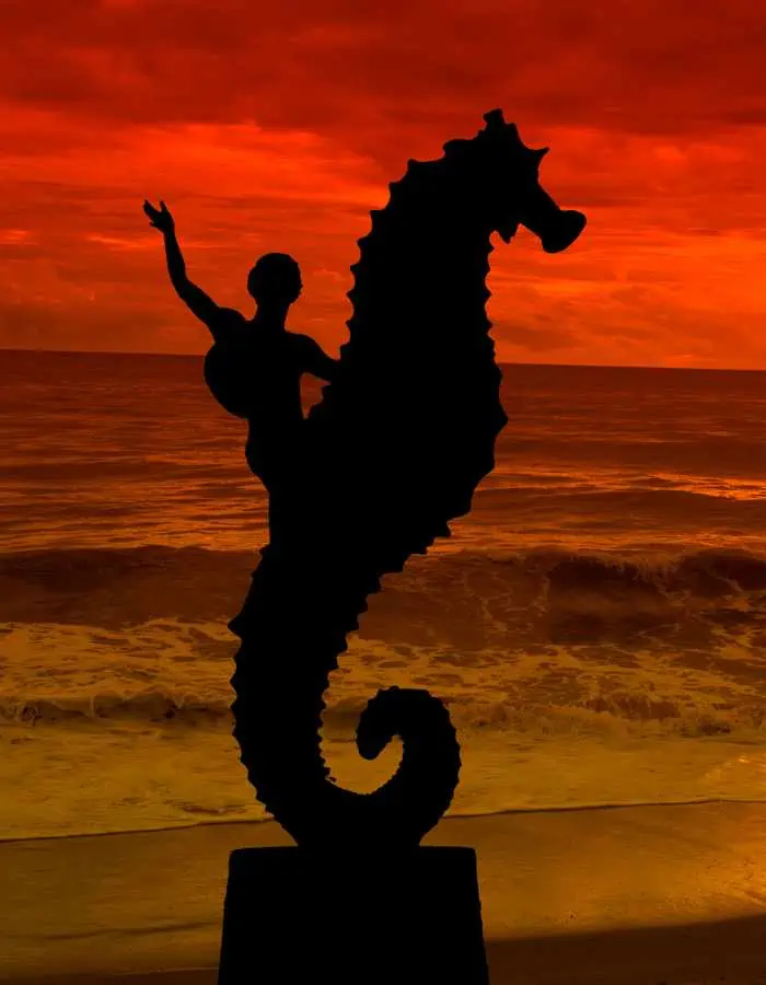 Silhouette of the iconic seahorse sculpture on the Puerto Vallarta shoreline, set against a dramatic sunset sky ablaze in shades of red and orange.