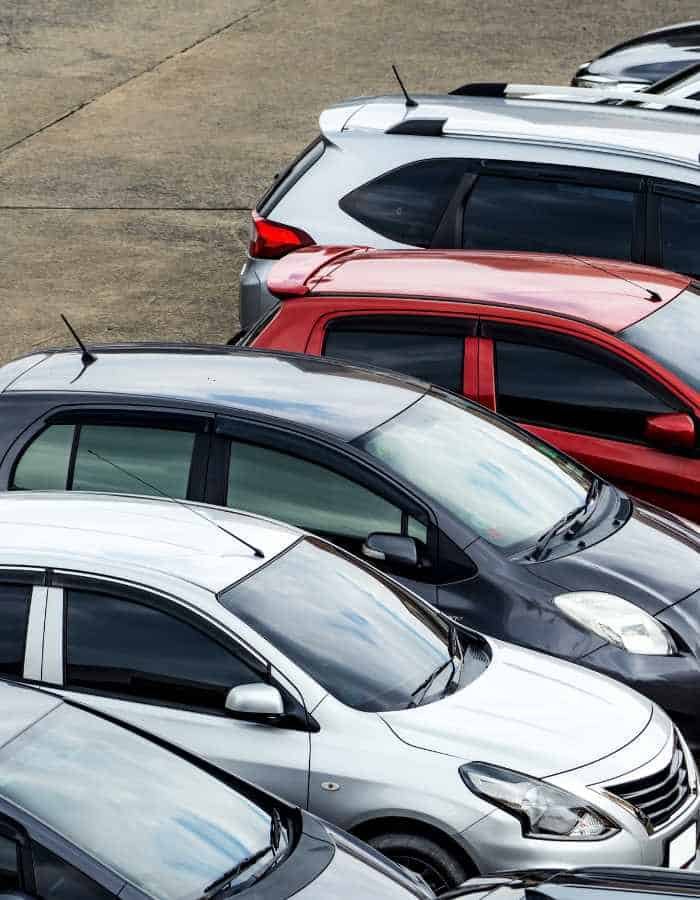 Aerial view of a variety of glossy rental cars in shades of white, silver, and red, neatly parked.