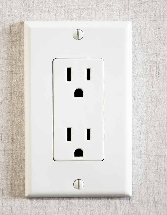 A white Type B electrical outlet mounted on a white wall plate against a textured gray background.