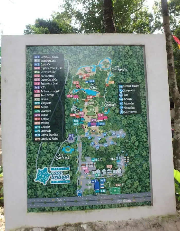 This image showcases a detailed map of Cenotes Casa Tortuga in Tulum, Mexico, displayed on a large sign. The map is color-coded and features various cenotes, lodging areas, restaurants, and activity zones surrounded by lush greenery. A legend on the left lists points of interest, including reception, parking, bars, restaurants, photography spots, kayak rentals, souvenir shops, security, and football fields.