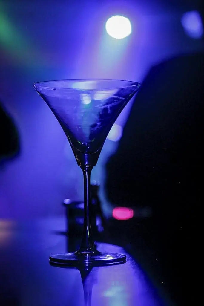 A crystal martini glass glows under vibrant nightclub lighting.