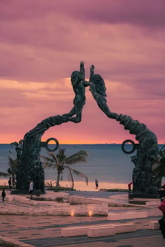 Beautiful sunset view of the Portal Maya Arch at Playa del Carmen with pink skies and ocean backdrop.